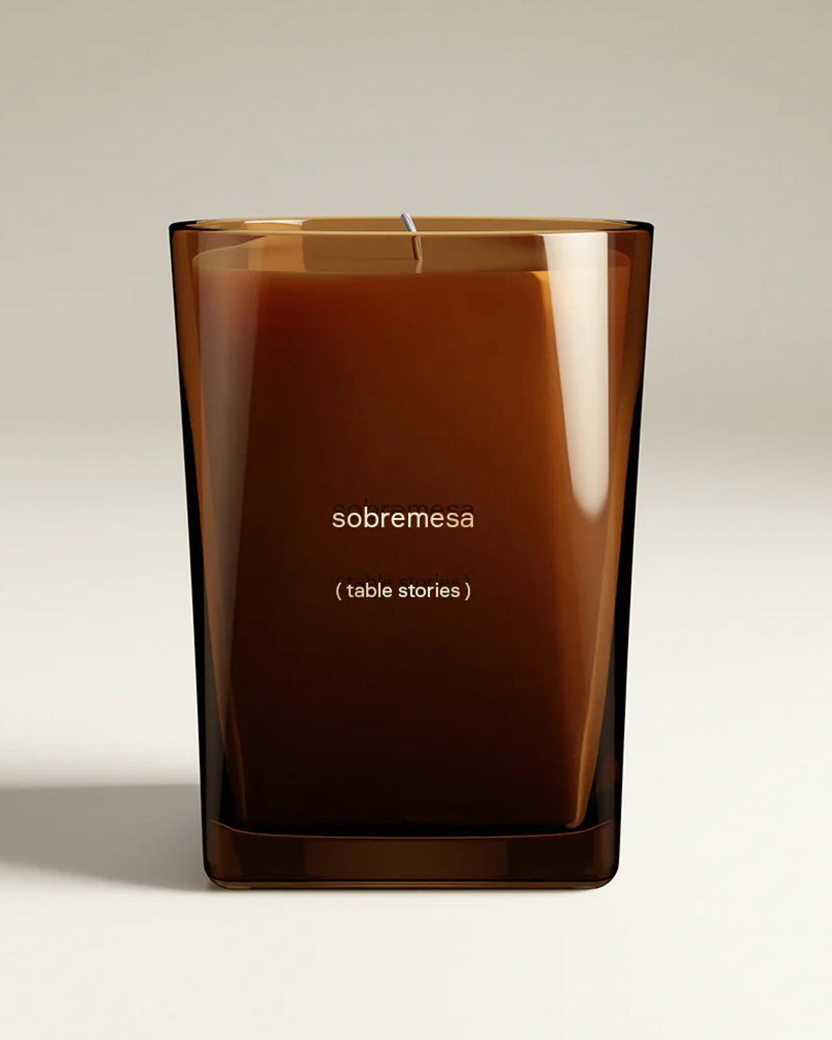 Luxury candle in a brown glass container, labeled 'sobremesa' on the front and, in parantheses, the definition: table stories, set on a white background. 