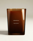 Luxury candle in a brown glass container, labeled 'sobremesa' on the front and, in parantheses, the definition: table stories, set on a white background. 