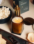 Luxury candle in a glass container on a table with popcorn and snacks
