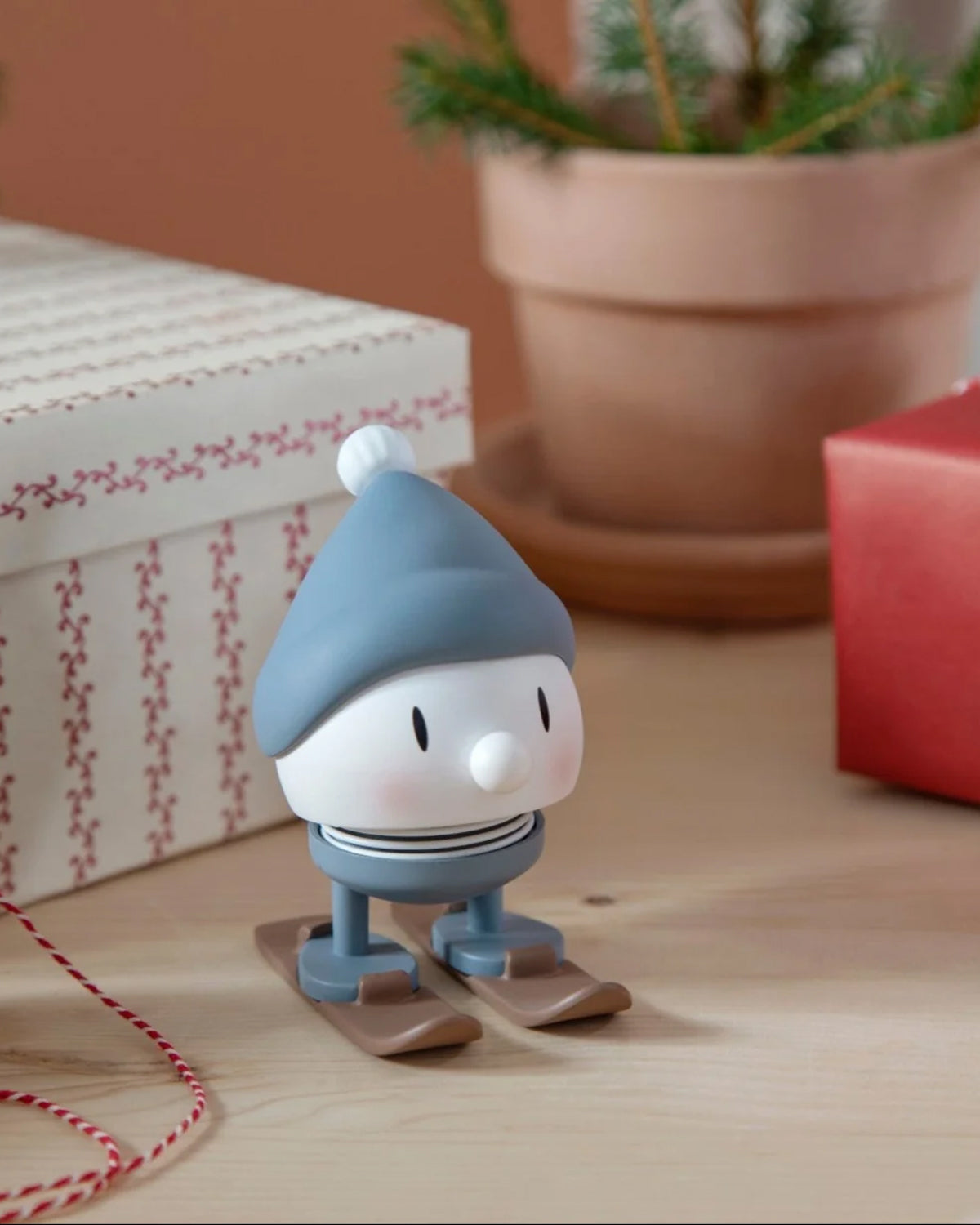 Blue-capped Hoptimist skier on a wooden table beside wrapped gifts and a potted fir