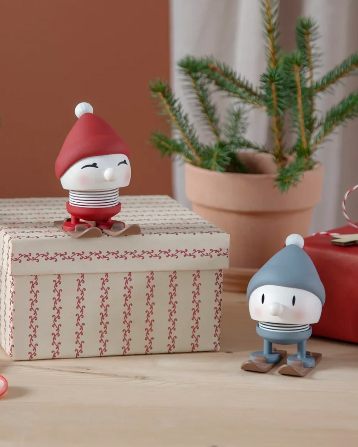 Red and blue Hoptimist skiing figures among wrapped gift boxes and a potted fir