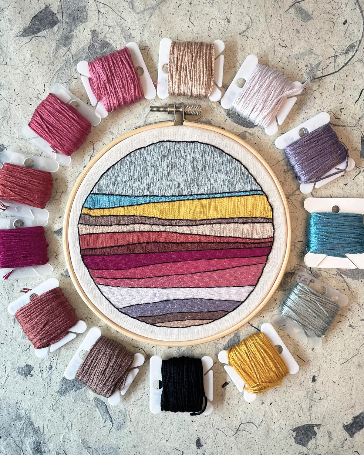 Landscape No. 2 embroidery in a 5-inch hoop, ringed by floss in pinks, golds and blues