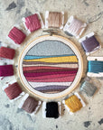 Landscape No. 2 embroidery in a 5-inch hoop, ringed by floss in pinks, golds and blues