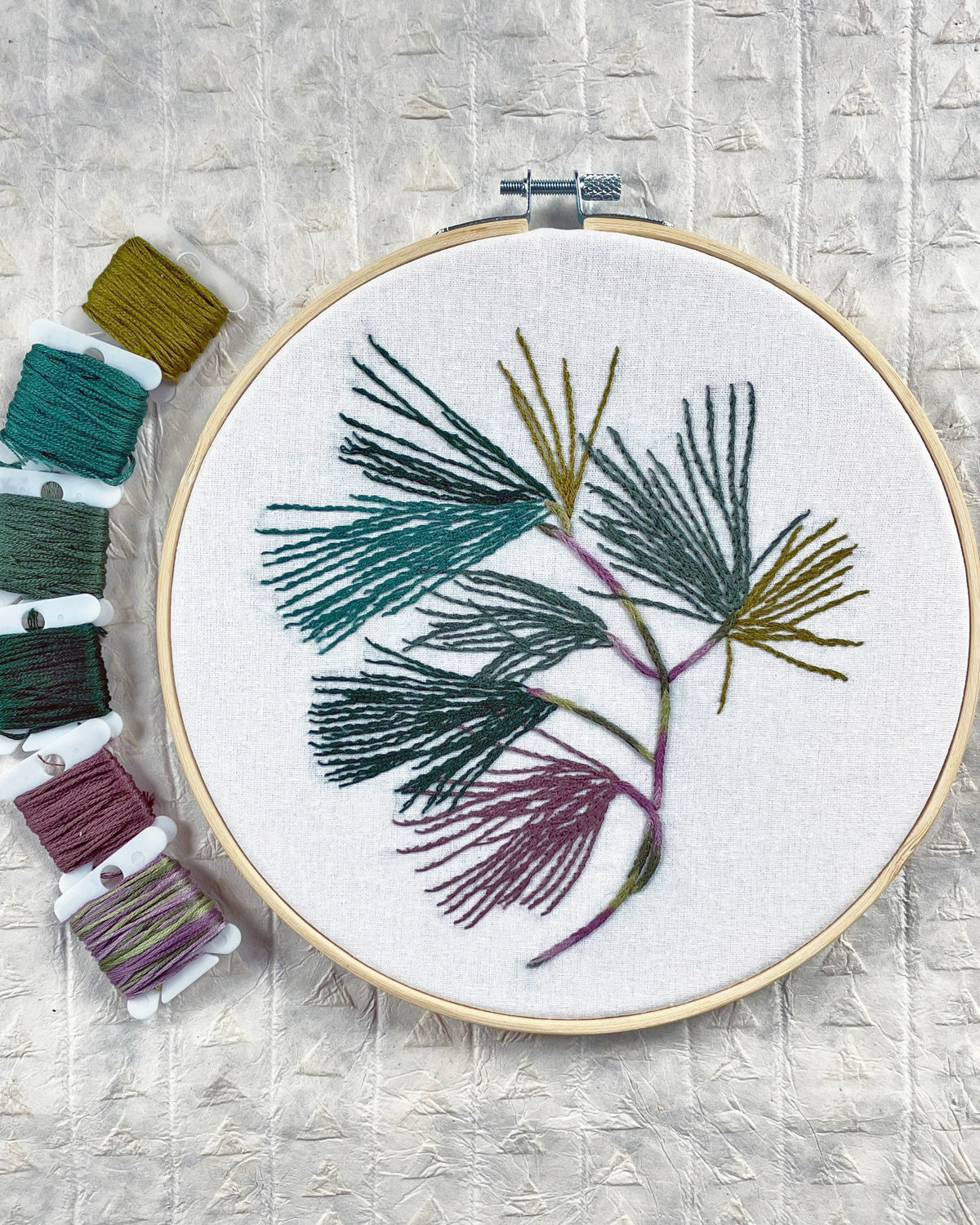 Finished Pine Boughs embroidery in teal, green and plum thread with floss bobbins