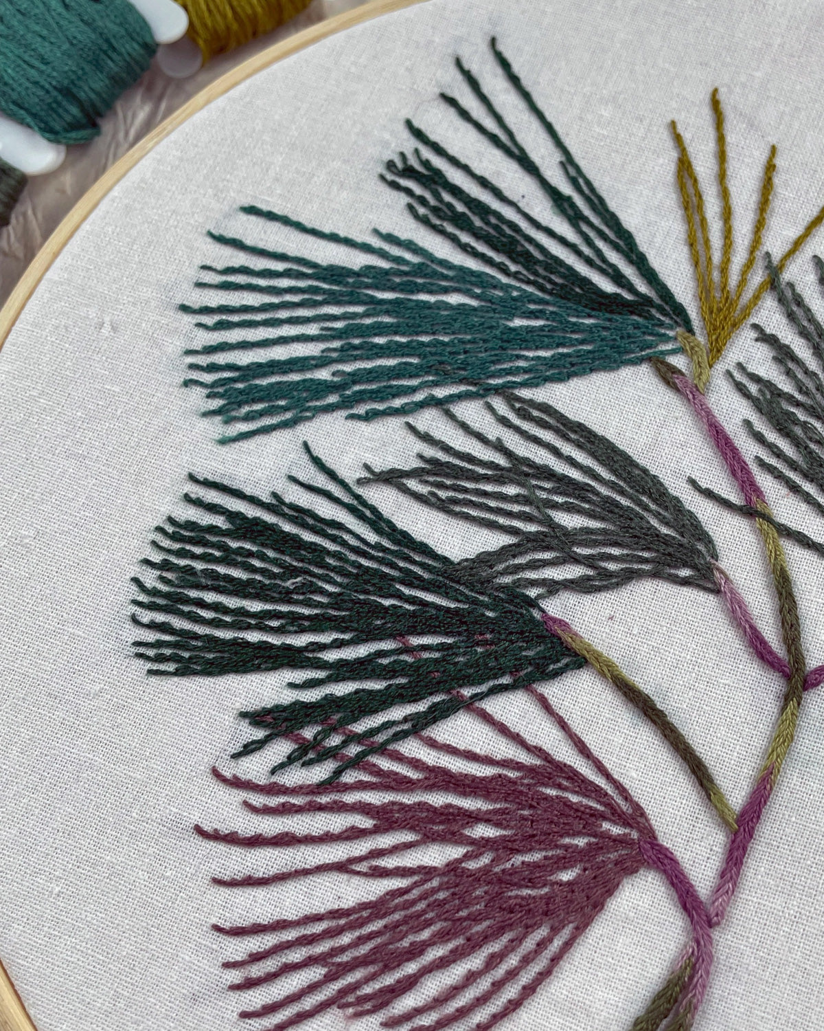 Close-up of stitched pine needles in teal, gray and plum on white fabric