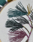 Close-up of stitched pine needles in teal, gray and plum on white fabric