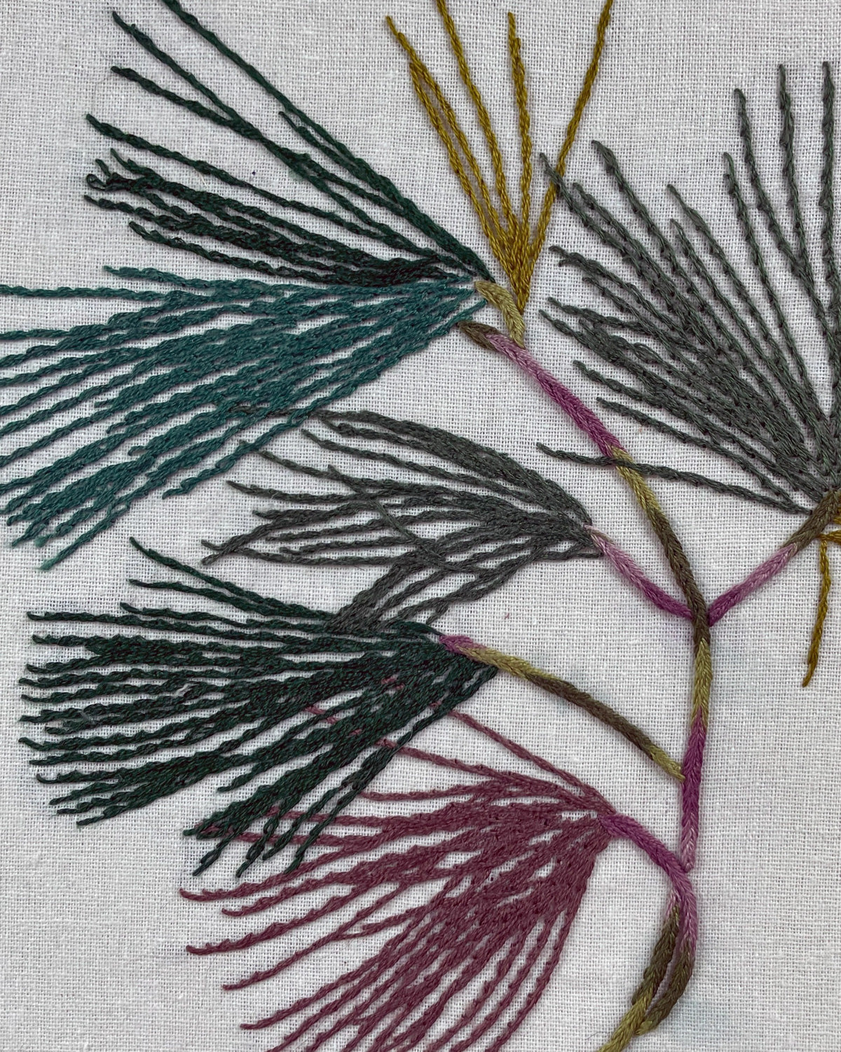 Close-up of the pine boughs stitching in deep green, mustard and dusty plum