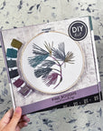 Hand holding the Kate Wyatt Pine Boughs DIY embroidery kit box