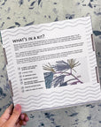 Back of the Pine Boughs kit box listing what's inside: floss, hoop, needle and fabric