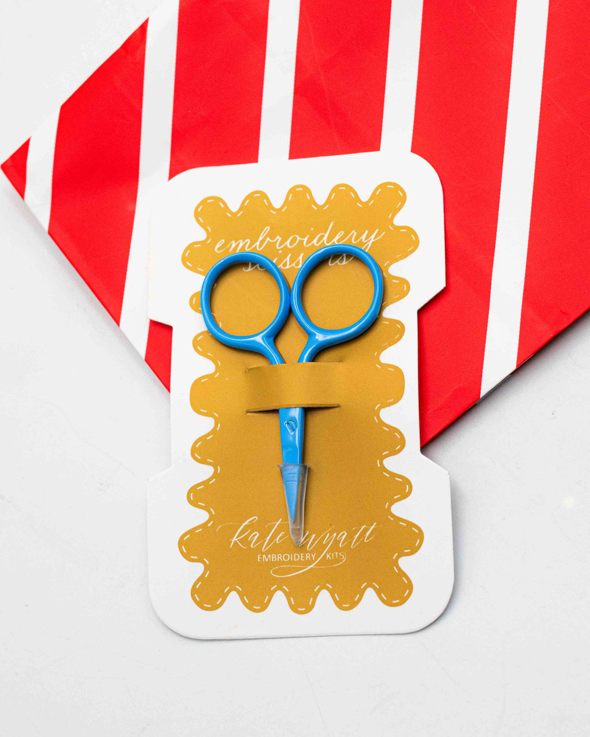 Kate Wyatt blue embroidery scissors on a mustard scalloped card, on red and white stripes