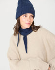 Model in a navy beanie and cream sweater wearing the navy Laolao cashmere mini scarf