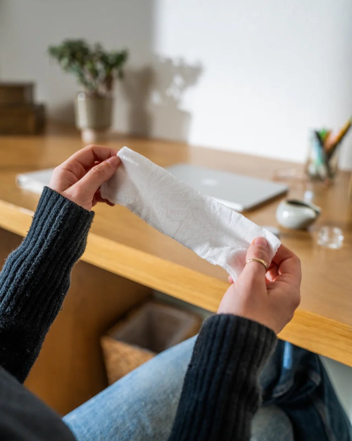 Person holding a 'Rest Your Eyes' aromatherapy eye towel in a home setting with a table and chairs in the background.