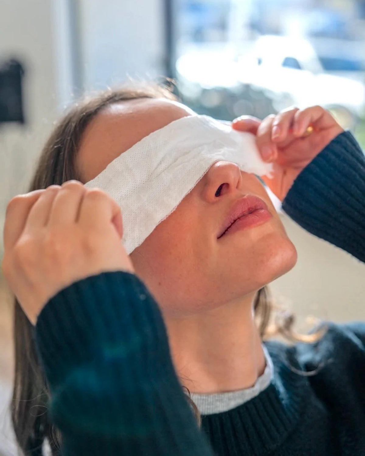 Person wearing a 'Rest Your Eyes' aromatherapy eye towel in an indoor, home setting.