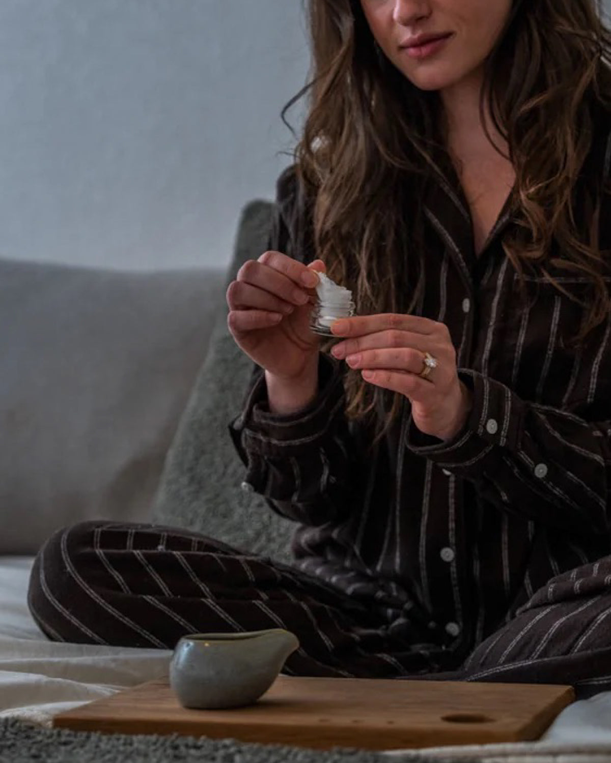 Woman in pajamas preparing the Rest Your Eyes aromatherapy eye towel on a bed.