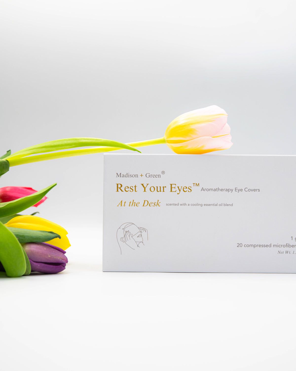 A gift box of 'Rest Your Eyes' aromatherapy eye covers with colorful tulips on a light gray background