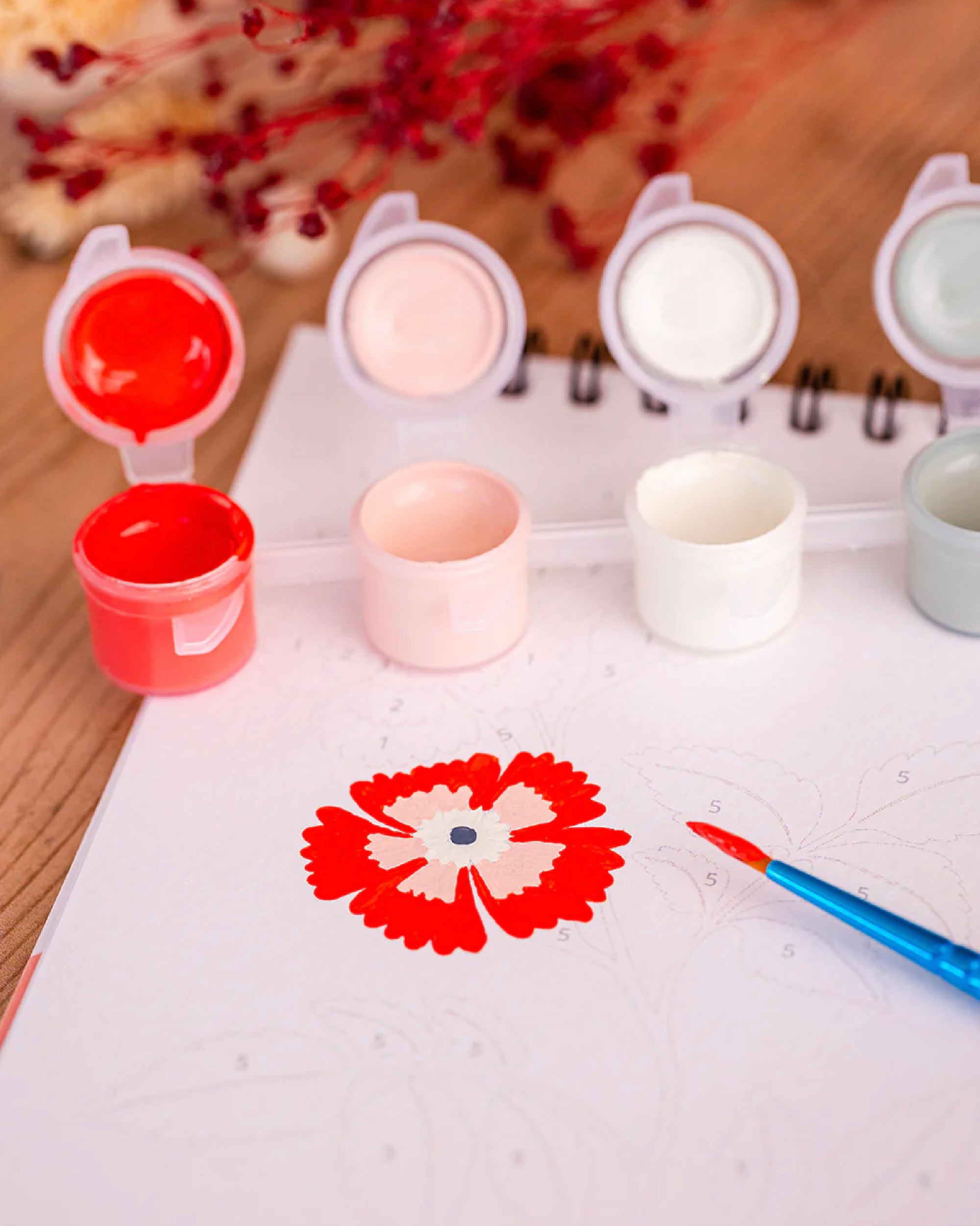 Set of small paint pots and a paintbrush with a floral design on paper