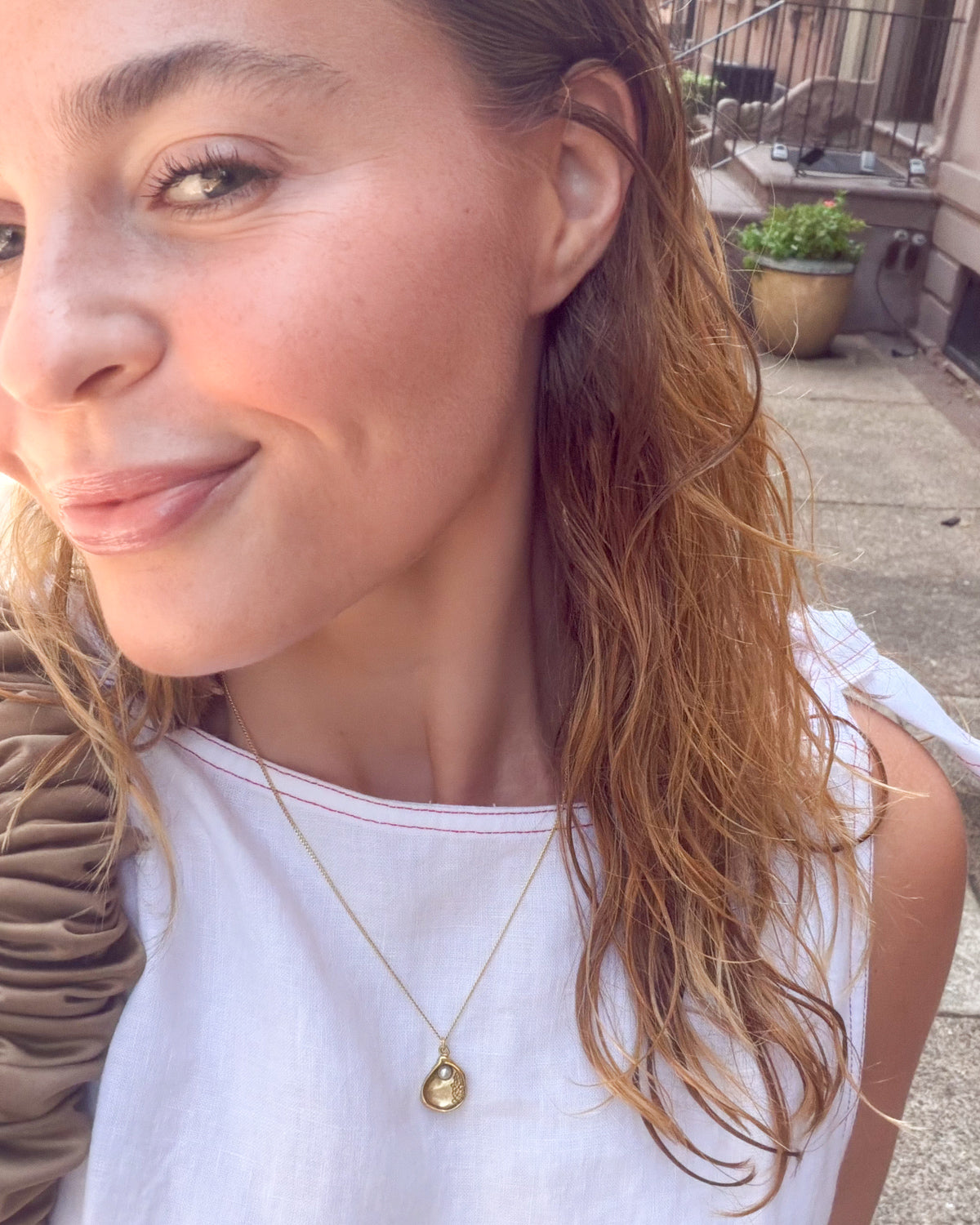 Woman wearing a gold necklace with a shell pendant outdoors