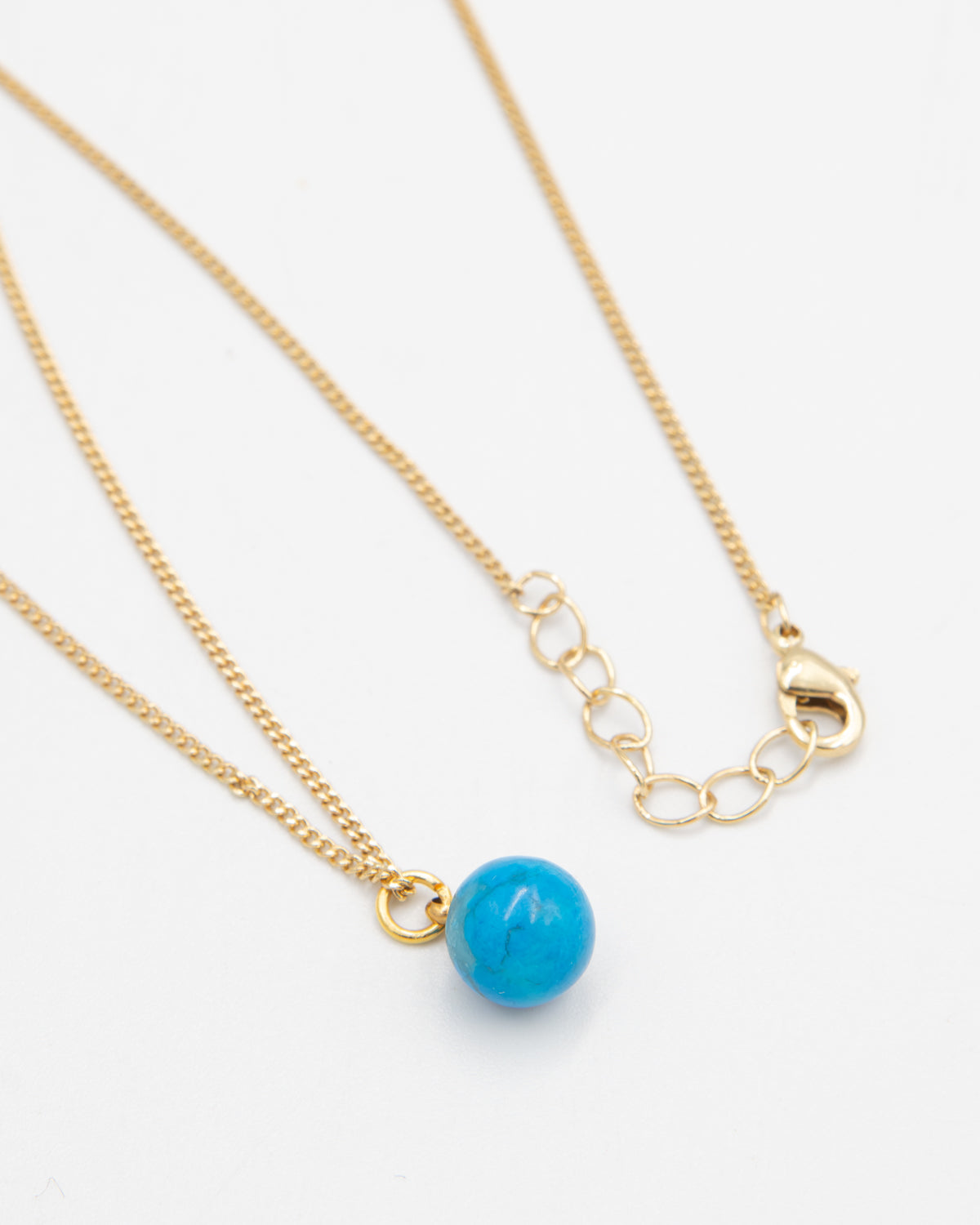 Gold necklace with a turquoise stone bead pendant on a white background