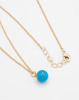 Gold necklace with a turquoise stone bead pendant on a white background