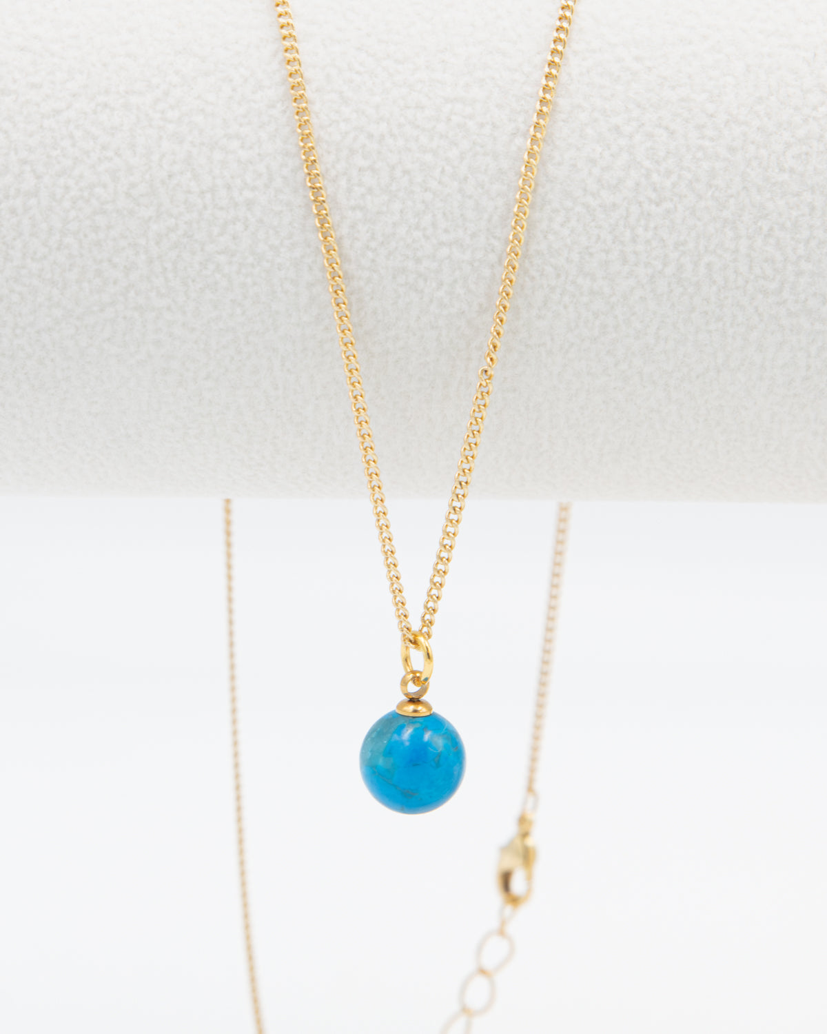 Gold necklace with a turquoise stone bead pendant hanging a white background
