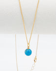 Gold necklace with a turquoise stone bead pendant hanging a white background
