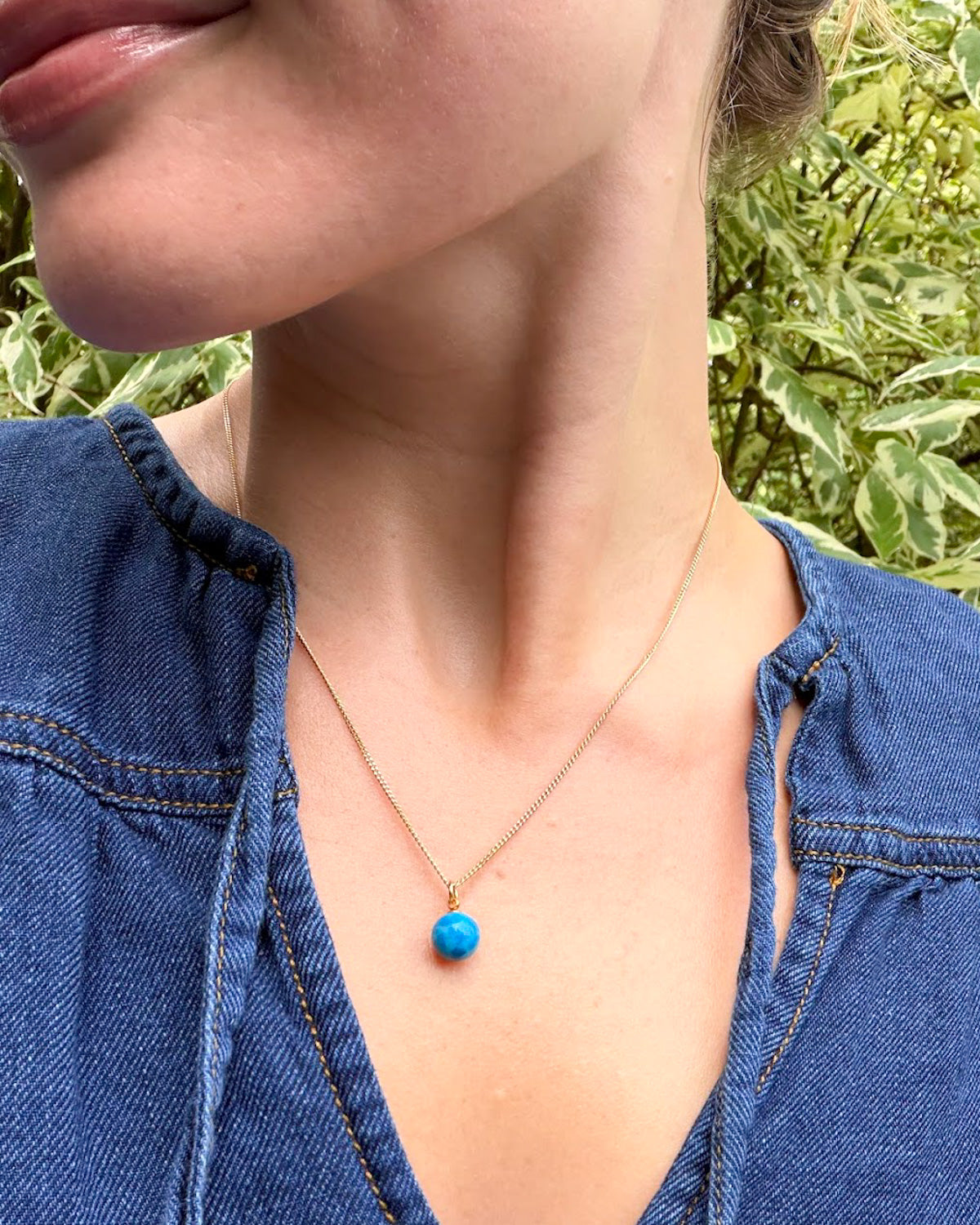 Person wearing a turqouise stone bead pendant necklace with a natural background