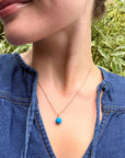 Person wearing a turqouise stone bead pendant necklace with a natural background
