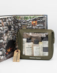 Army green travel pack with Mayron's Goods products in front of an opened book with a stone fireplace image.