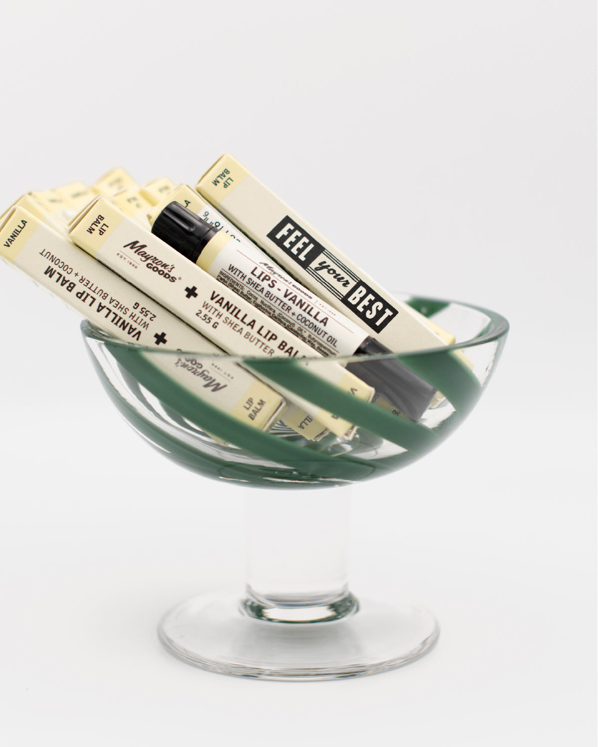 Coupe glass with a tube of Mayron&#39;s Goods Vanilla Lip Balm mixed with 9 tubes in boxes