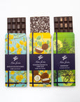 Three Milene Jardine dark chocolate bars partly unwrapped: lemon, coconut and rosemary