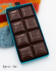 Close-up of an opened Miss Maude’s Aprés Ski dark chocolate bar with eight flavored squares displayed on a colorful knit hat 