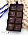 Close up of open box of Miss Maude's Whiskey Business dark chocolate bar, featuring 8 squares with difffent flavors on a white and beige knit background 