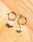 Nach Bijoux Daydreamer gold hoops with white porcelain cloud and moon charms on wood