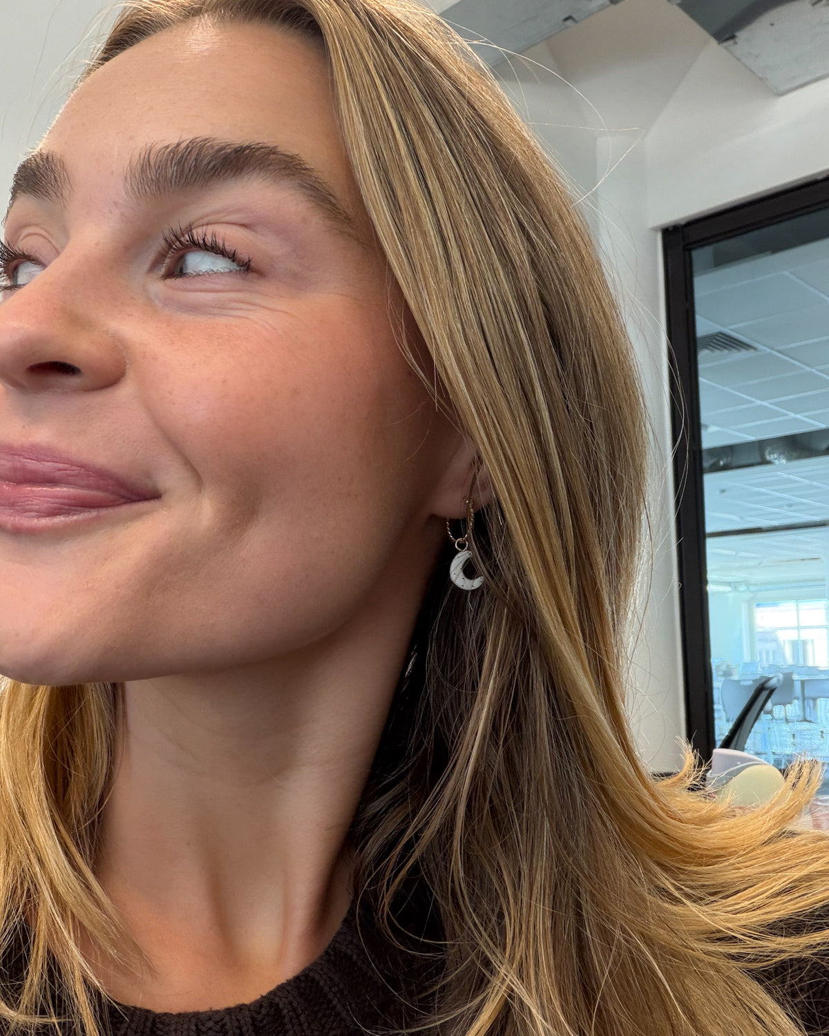 Smiling woman wearing a Daydreamer gold hoop with a small white moon charm