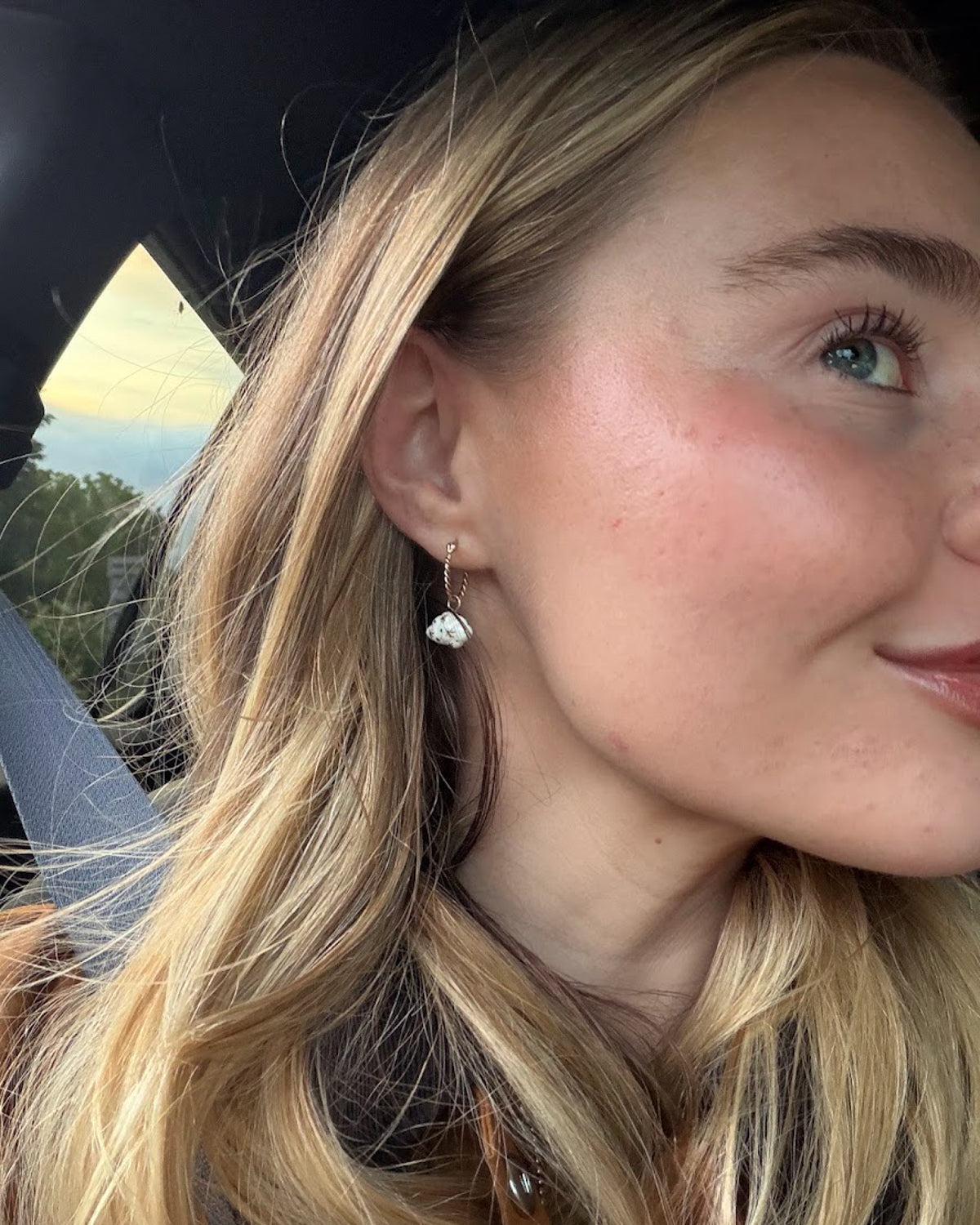 Woman in a car wearing a Daydreamer mini hoop earring with a white porcelain cloud charm