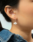 Close-up of an ear wearing a Daydreamer gold hoop with a white cloud charm, with a denim jacket