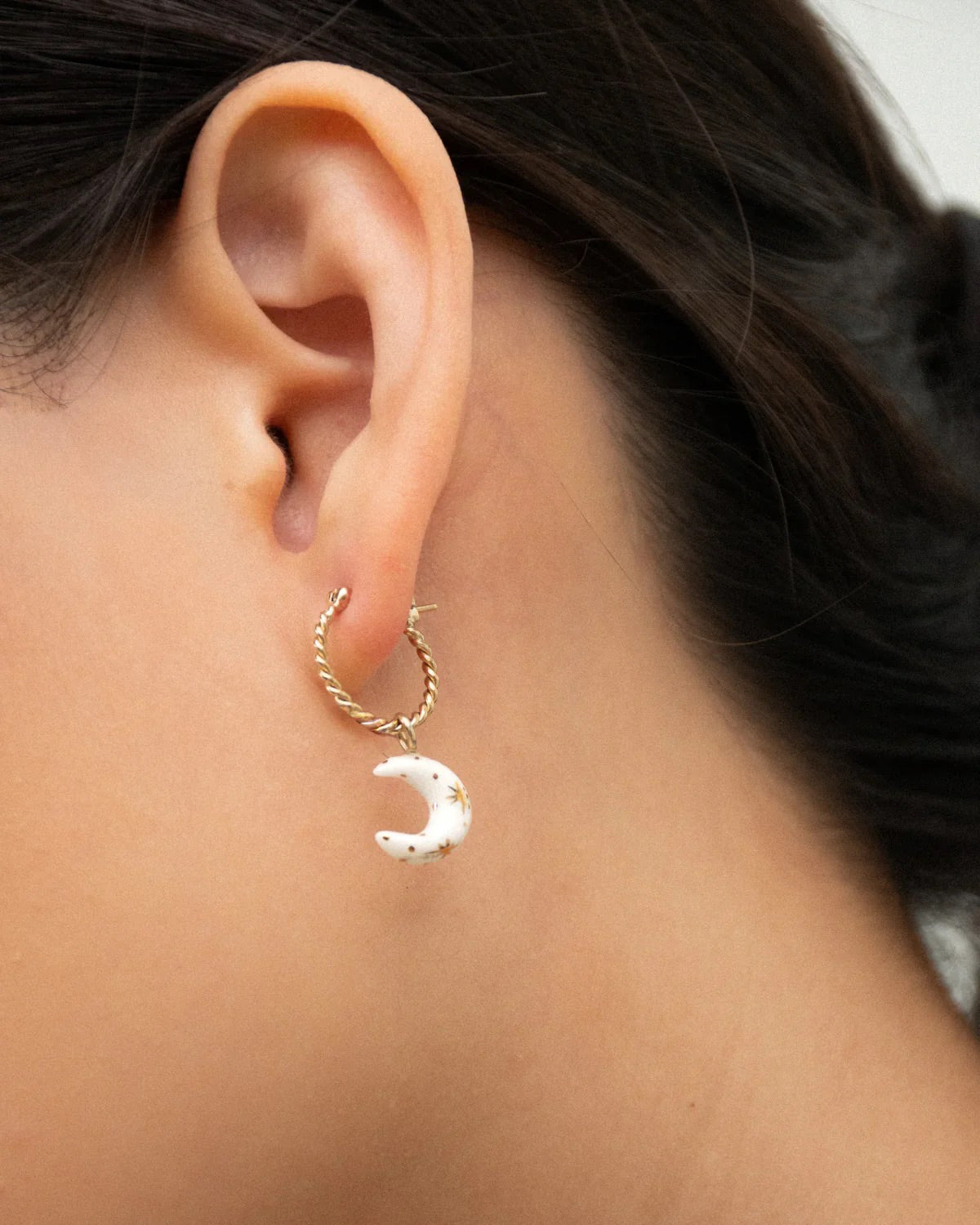 Close-up of an ear wearing a twisted gold mini hoop with a white porcelain crescent moon