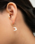 Close-up of an ear wearing a twisted gold mini hoop with a white porcelain crescent moon