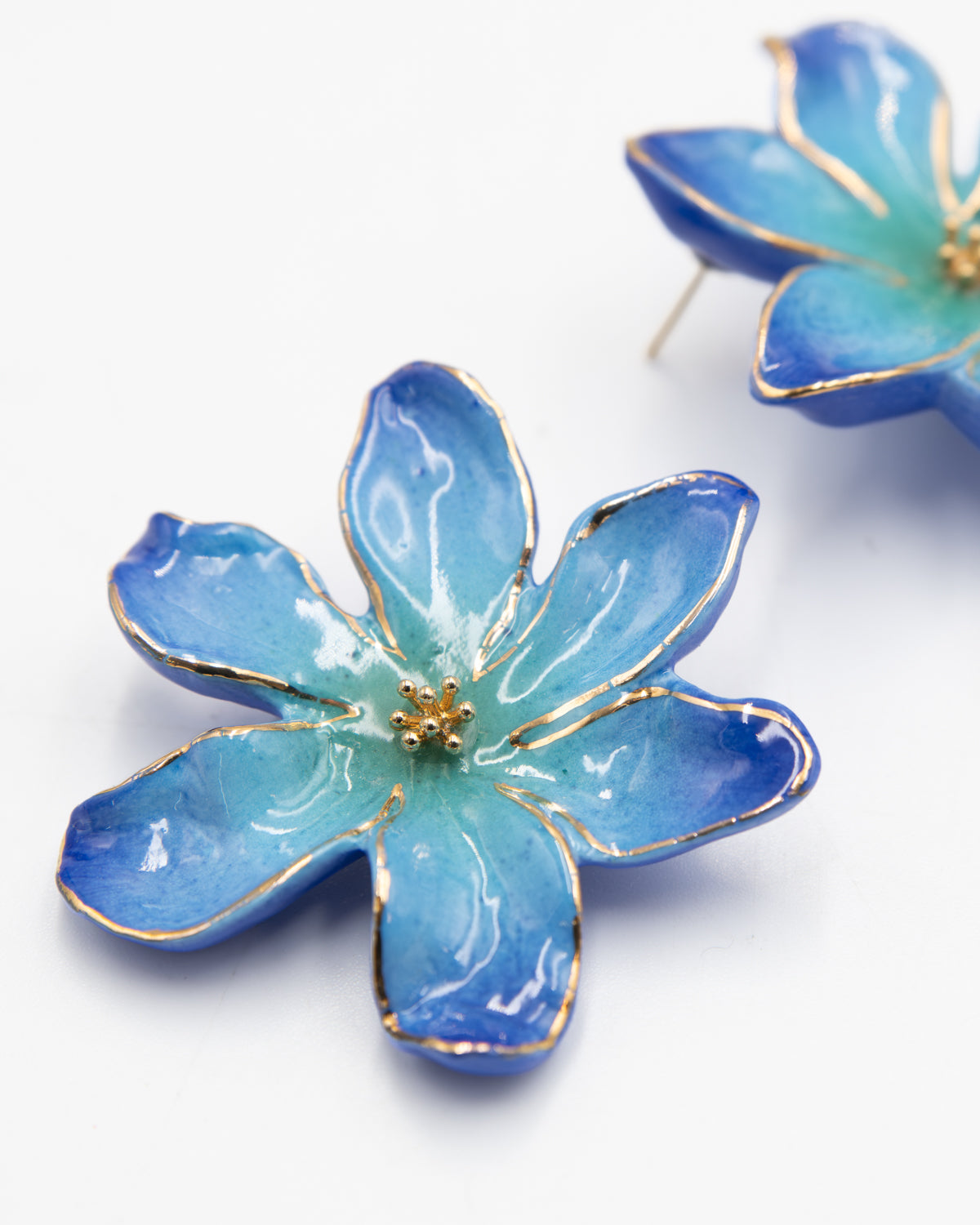 Close-up of Frost Flower porcelain earrings with blue petals outlined in gold