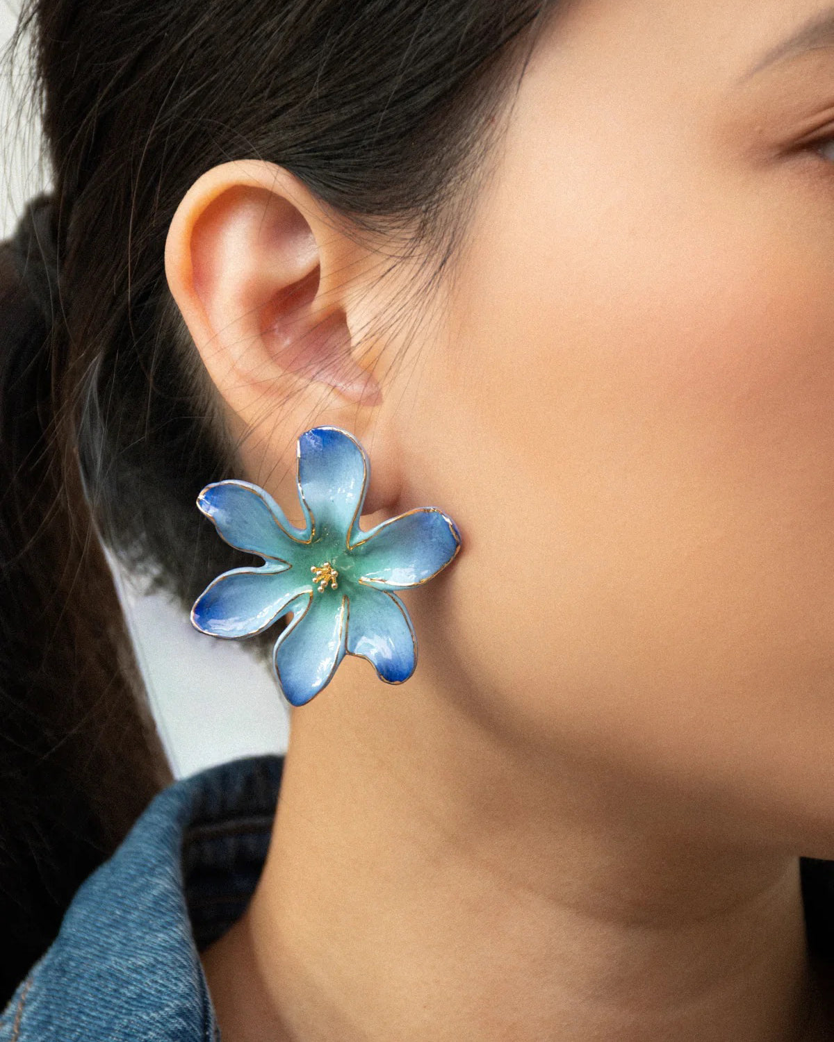 Close-up of an ear wearing the Frost Flower earring in blue and aqua with a gold center