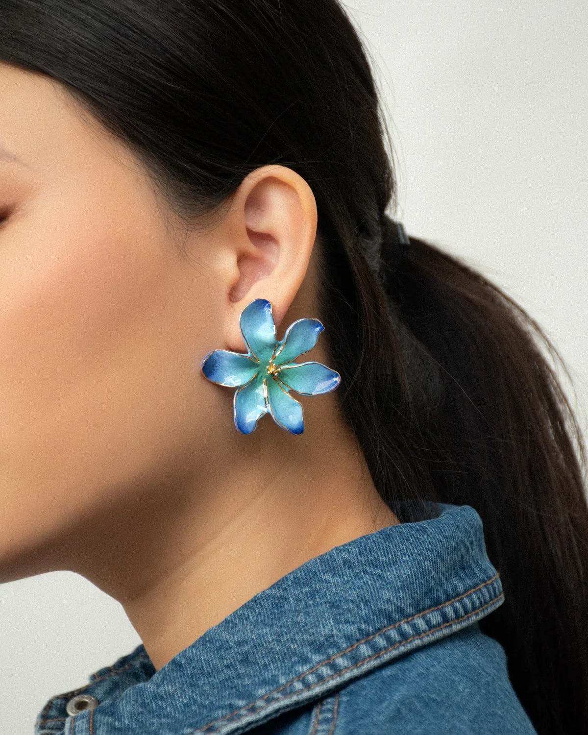 Woman with a ponytail and denim jacket wearing a blue porcelain Frost Flower earring