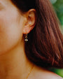 Close-up of a person wearing lightweight gold earrings with a small porcelain bee drop.