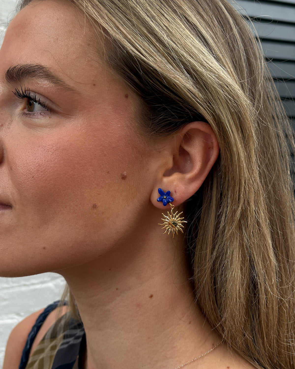 Woman wearing a Once in a Blue Moon earring with a blue flower stud and gold sun charm