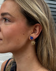 Woman wearing a Once in a Blue Moon earring with a blue flower stud and gold sun charm
