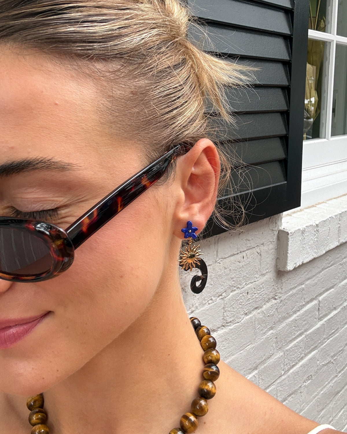 Woman in tortoiseshell sunglasses wearing the blue flower and gold sun drop earring