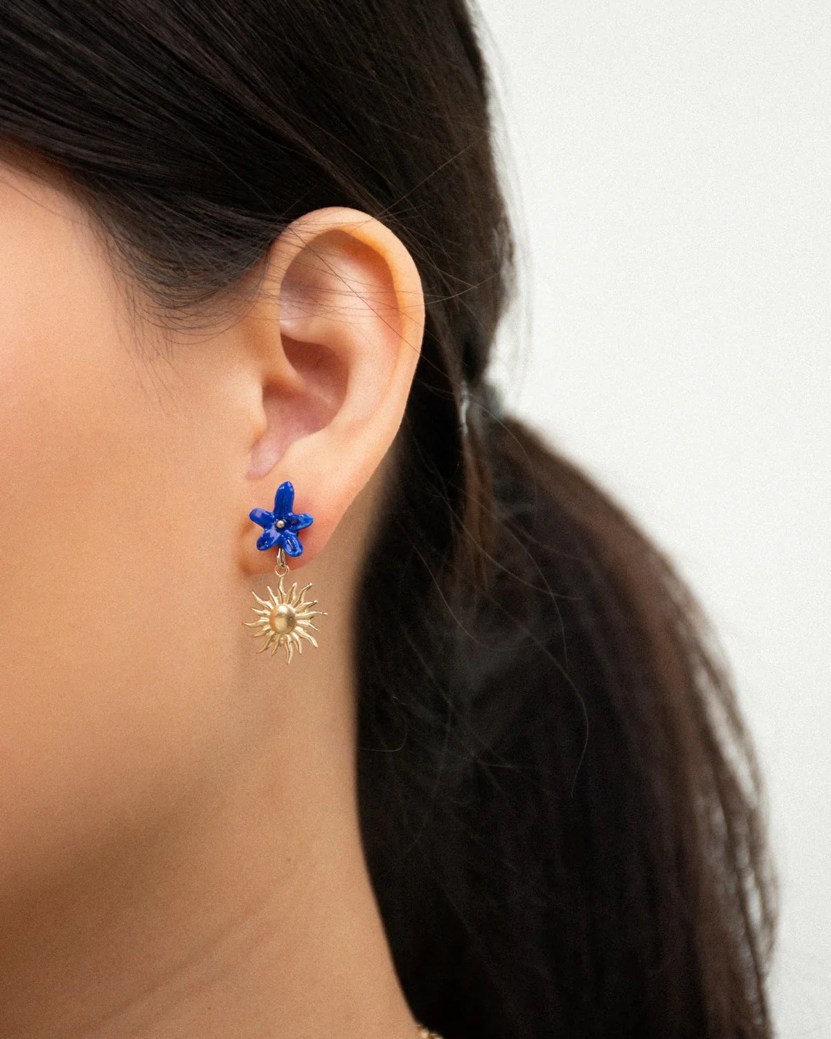 Close-up of an ear wearing a blue porcelain flower stud with a small gold sun drop