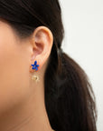 Close-up of an ear wearing a blue porcelain flower stud with a small gold sun drop