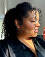 Woman with curly hair wearing a black shirt and hand-painted, porcelain and gold flower-shaped hoop earrings 