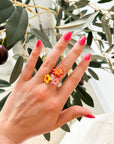 Nach Bijoux's hand-painted porcelain floral and gold ring on a person's hand with a plant in the background