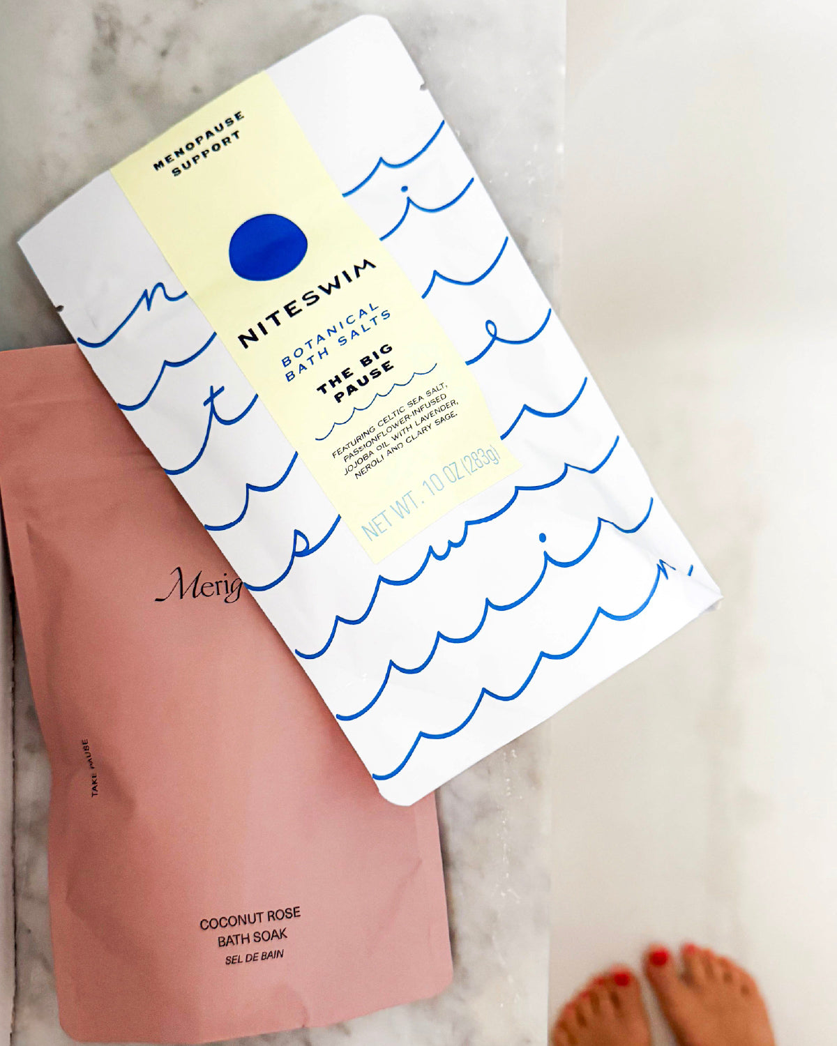 Niteswim The Big Pause bath salts pouch with a wave print, lying on a pink Merigold pouch